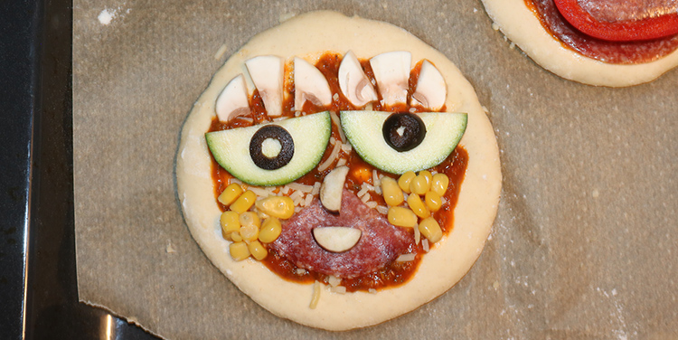 Pizzetten mit Gemüse zu Gesichtern legen